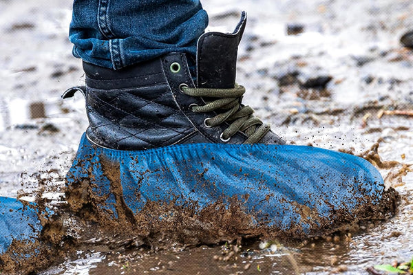Blue shoe covers over work boots on a muddy floor