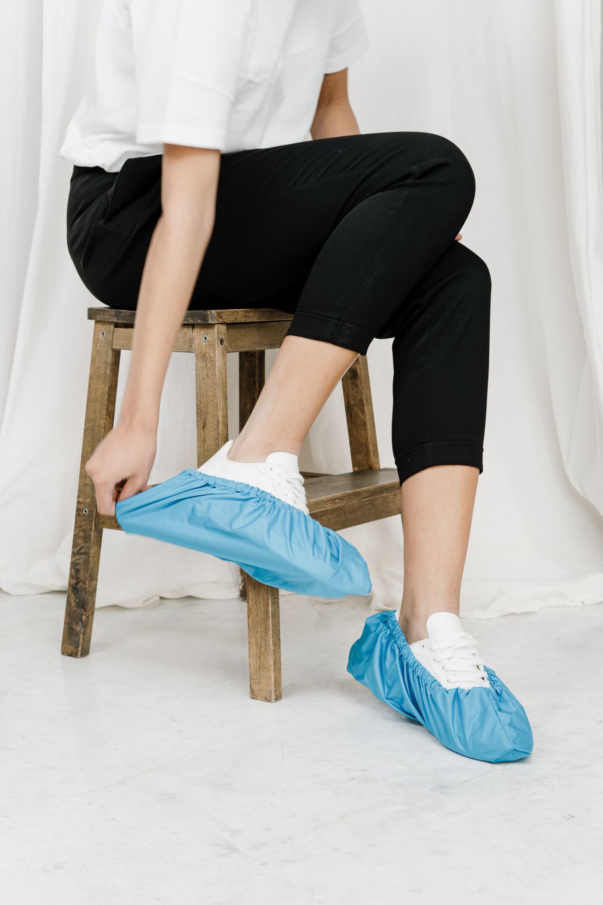 Person sitting indoors wearing blue disposable shoe covers over sneakers