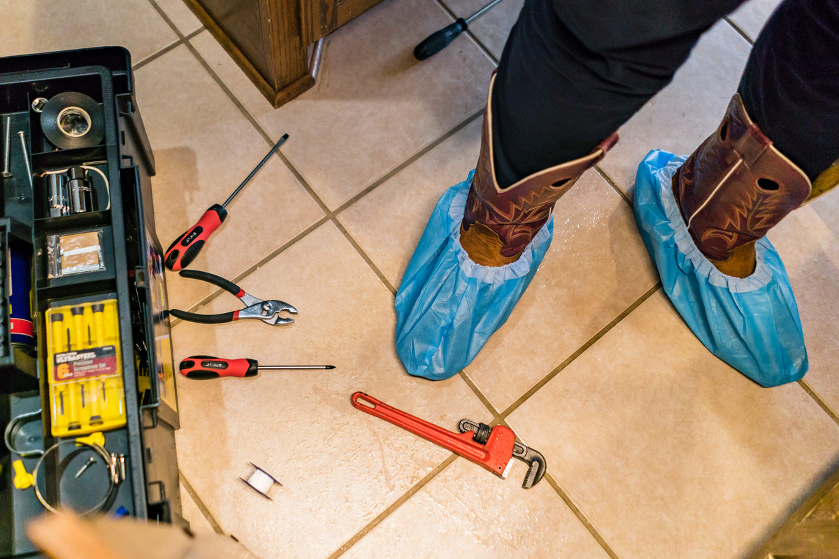Plumber wearing Blue Shoe Guys covers over boots on a clean tile floor
