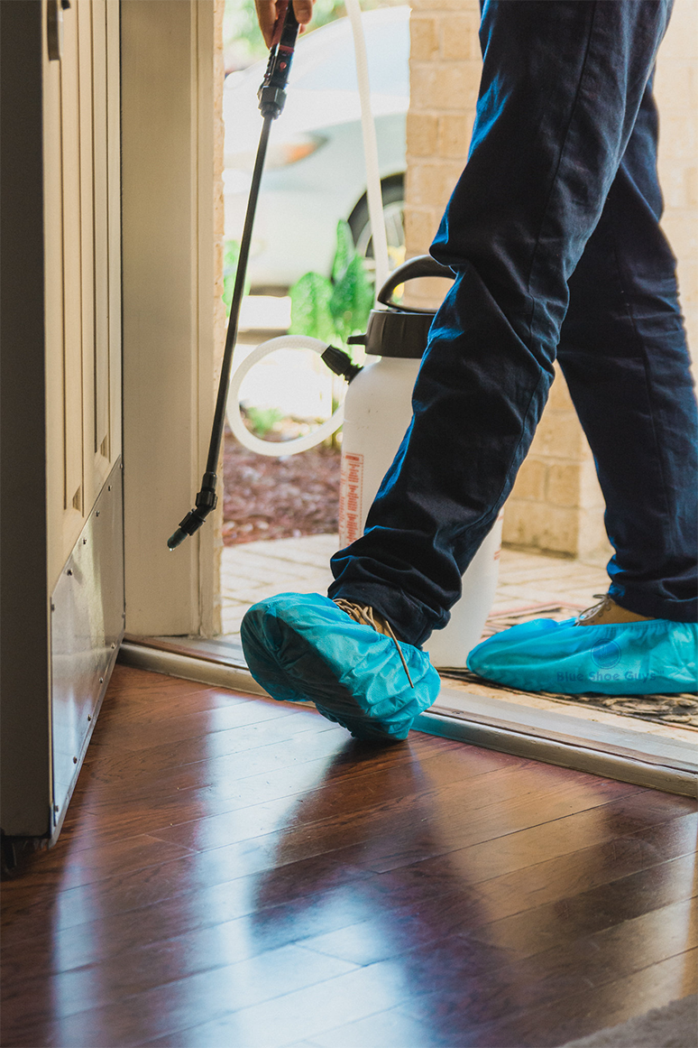 Pest control tech in shoe covers stepping onto a hardwood floor